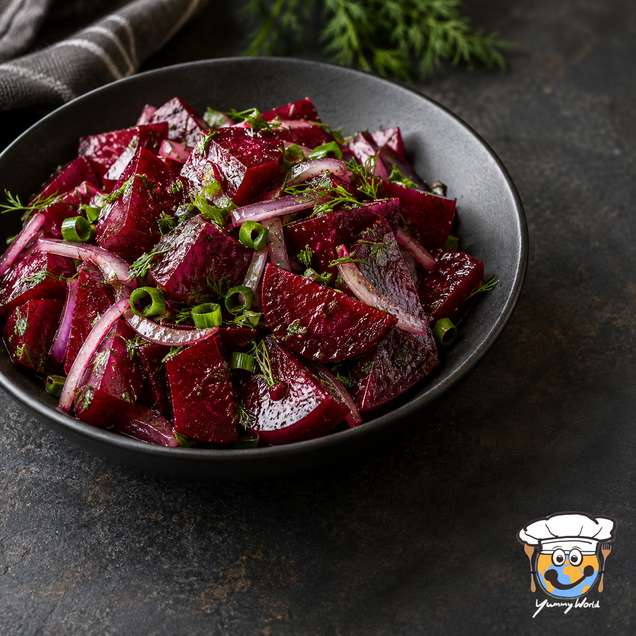 Klassischer Rote-Bete-Salat mit roten Zwiebelscheiben und gehackten grünen Kräutern in einer schwarzen Schale.