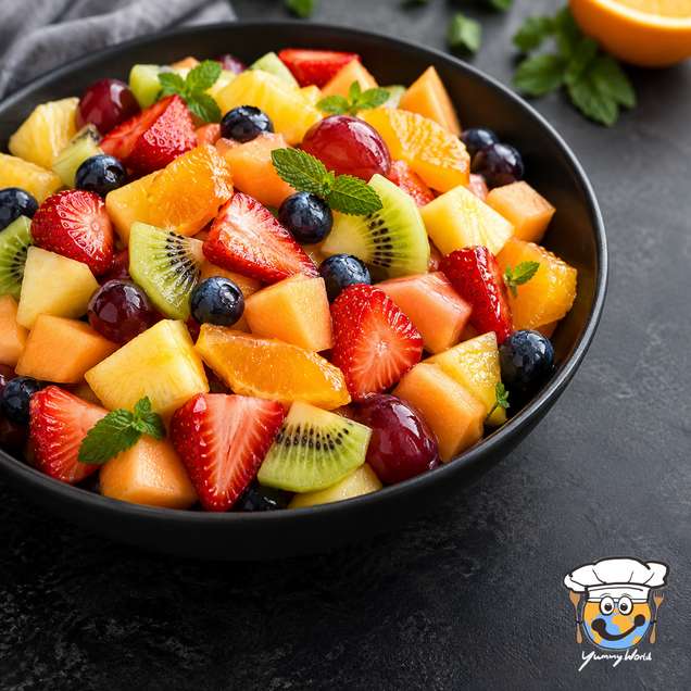 Colorful fruit salad with strawberries, kiwi, melon, pineapple, orange and blueberries in a black bowl.